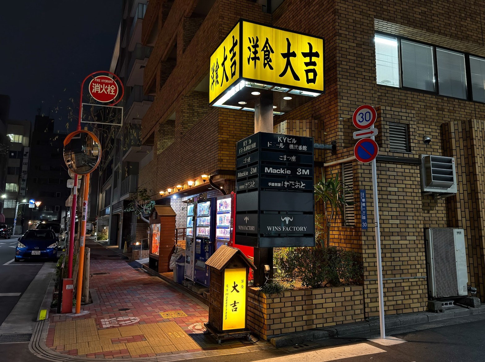 夜の「洋食 大吉」黄色い正方形看板が点灯し、周囲のビル案内板や自動販売機が並ぶ柳橋の路地角